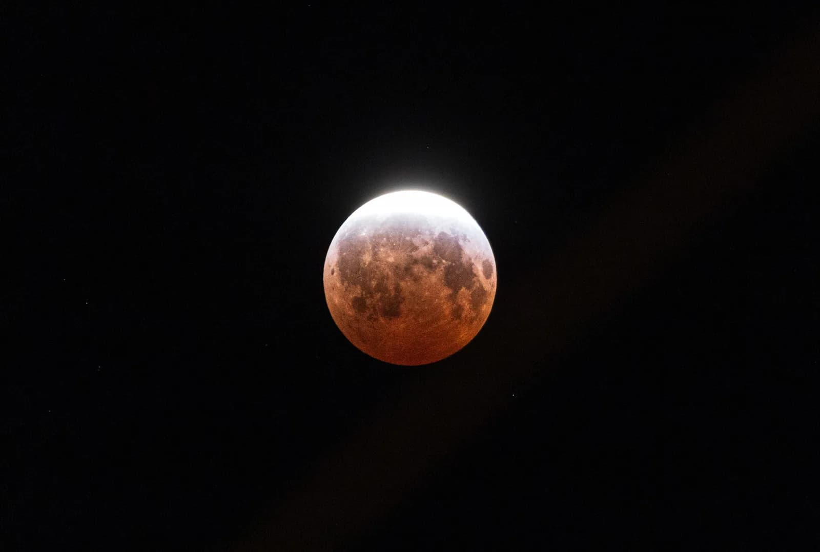 La luna cobriza casi cubierta por la sombra de la Tierra, con una uña de luz brillando en el borde, durante el eclipse del 28 de agosto de 2026