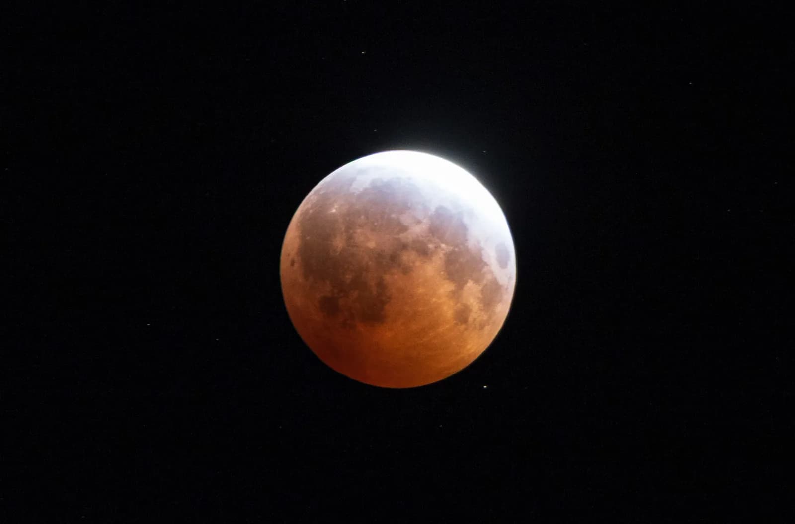 La luna cobriza casi cubierta por la sombra de la Tierra, con una uña de luz brillando en el borde, durante el eclipse del 28 de agosto de 2026