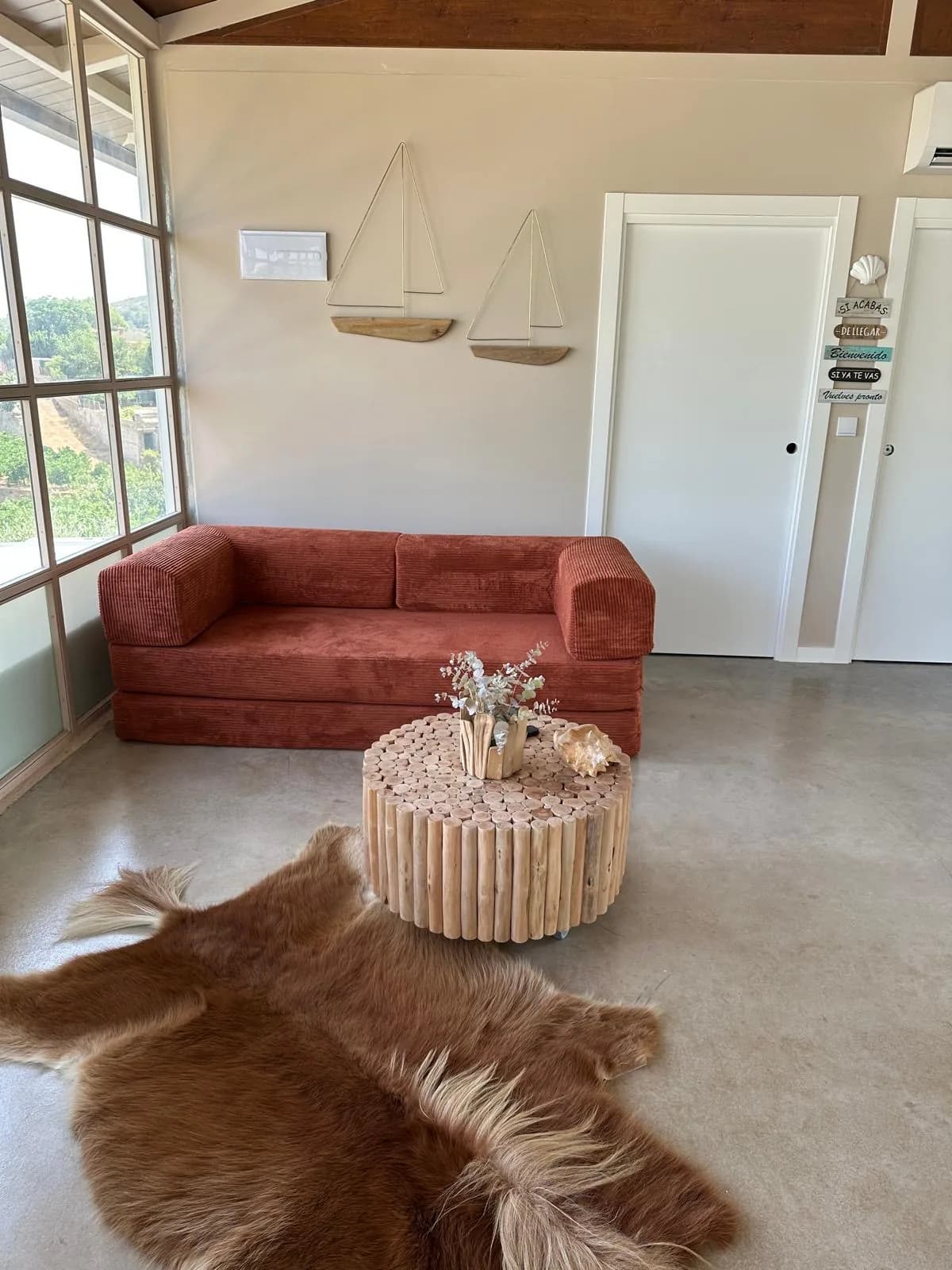 Zona de estar con sofá terracota, mesa de madera y ventanal lateral