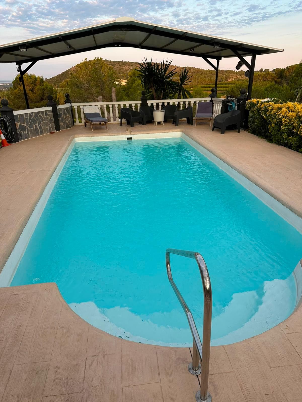 La piscina bajo la pérgola, con las tumbonas y la balaustrada blanca mirando al valle