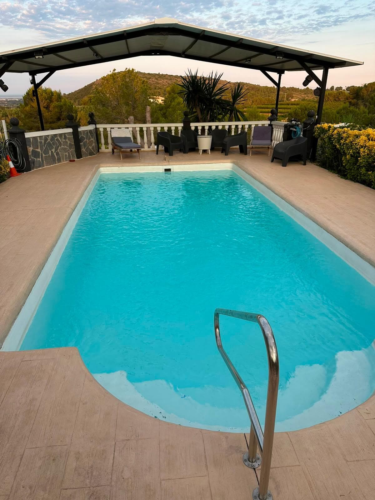 La piscina completa bajo la pérgola al atardecer, con la montaña y los campos detrás